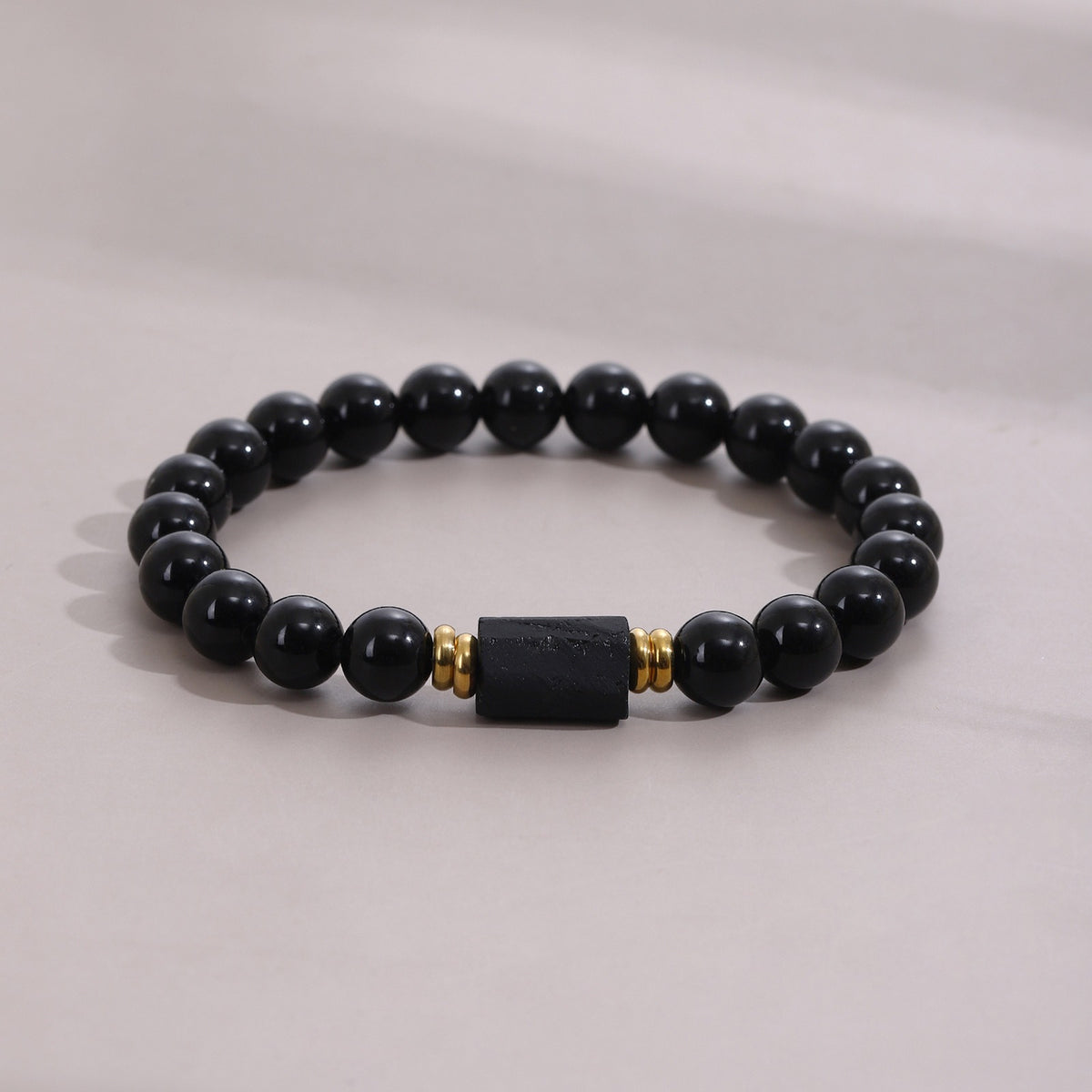 Bracelet en obsidienne noire posé à plat, anneaux dorés