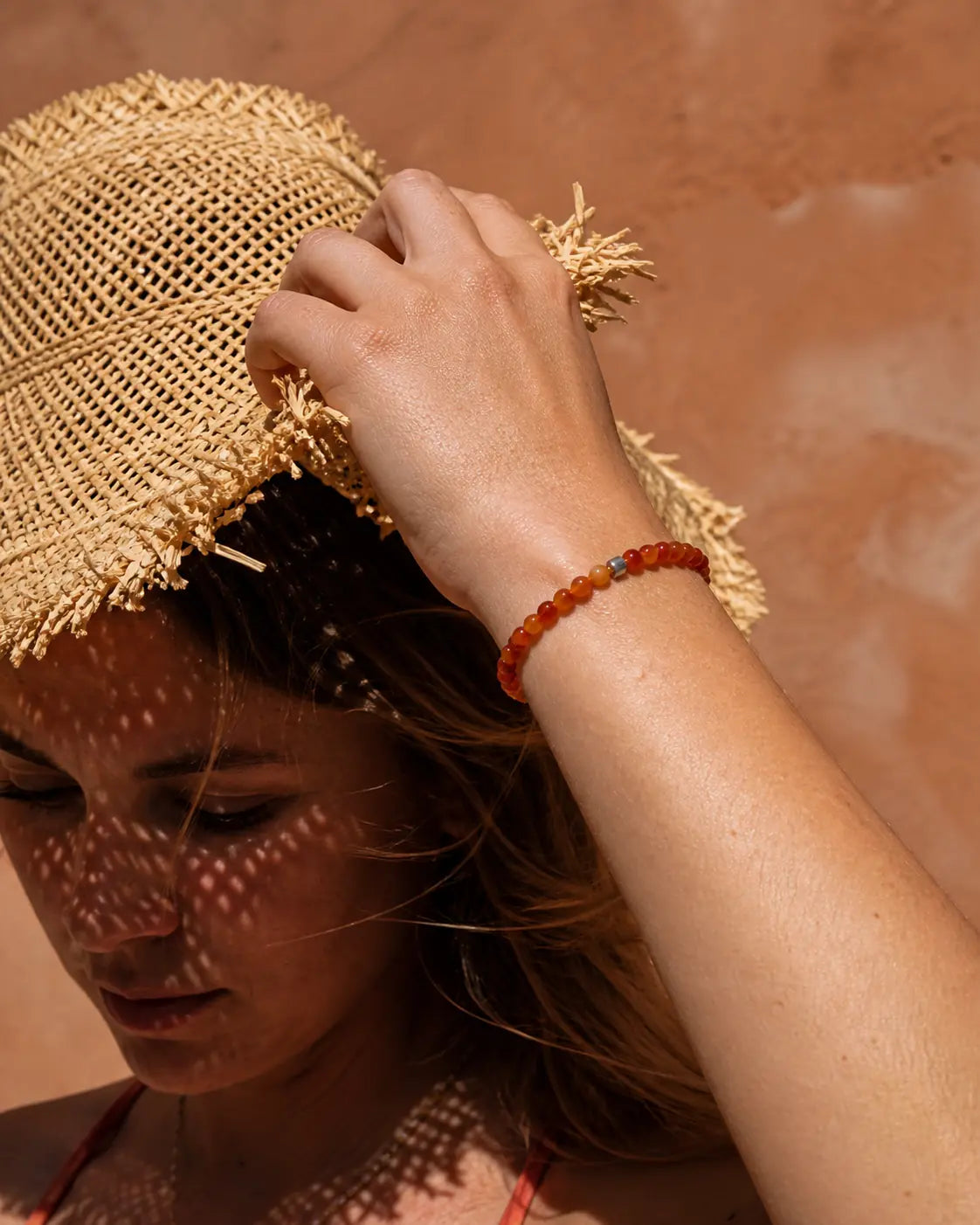 Femme portant un mini bracelet en cornaline, chapeau de paille, plein soleil d'ete