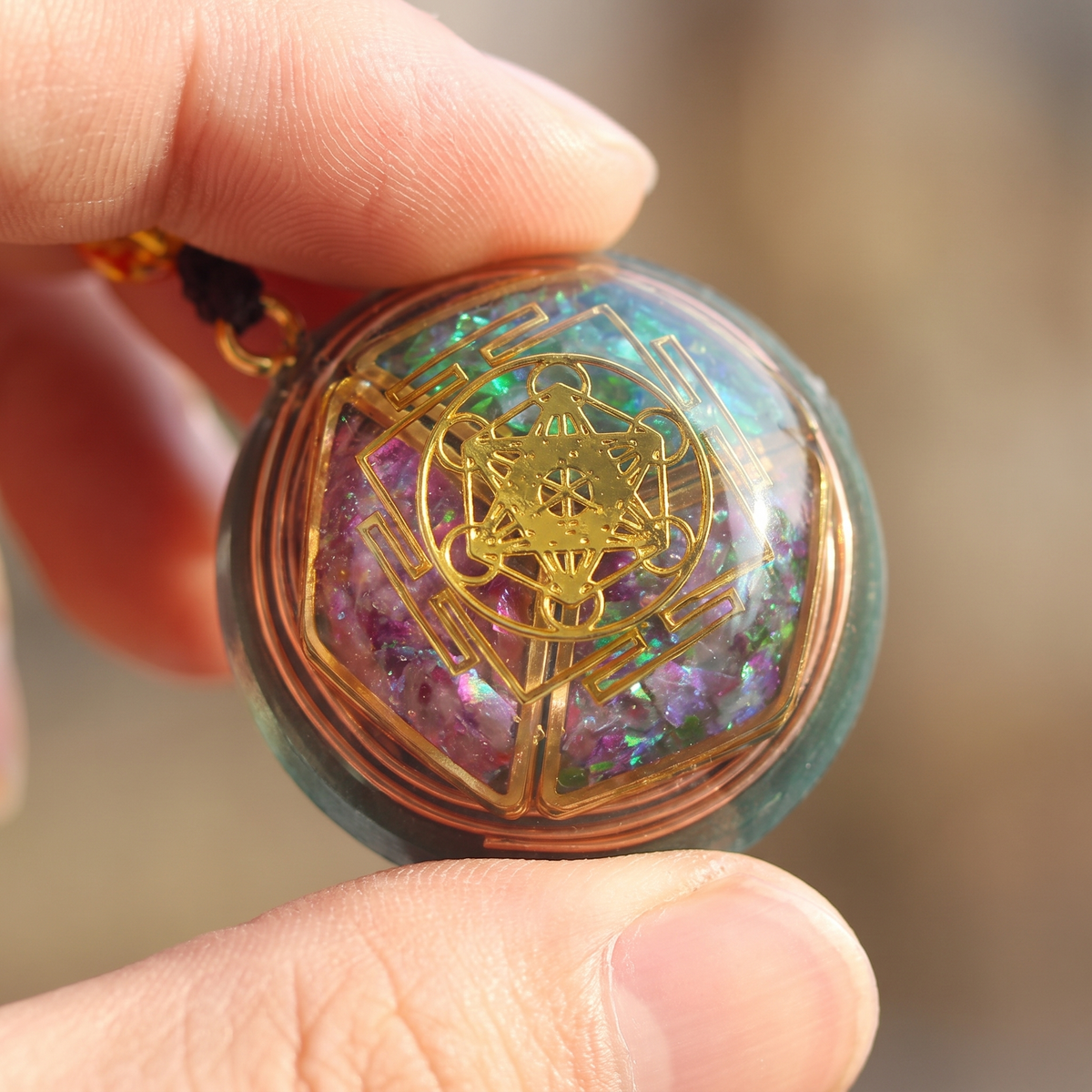 Macro du pendentif orgonite entre les doigts, cube de Métatron doré